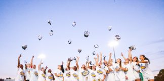 Female soccer league champions throw hats in the air while surrounding SEC trophy