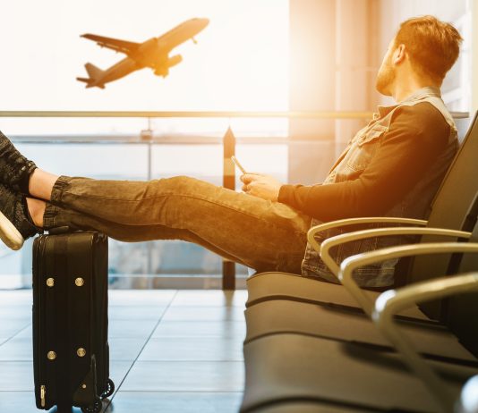 Man sitting at airport watching a plane fly